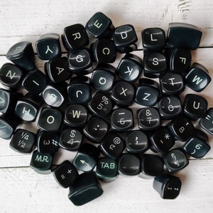 May include: A collection of black typewriter keys with white lettering. The keys feature letters, numbers, punctuation marks, and symbols.
