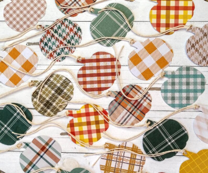 May include: A collection of 16 fall-themed pumpkin-shaped paper cutouts with various plaid patterns in shades of green, brown, orange, and white. The cutouts are strung together with twine.