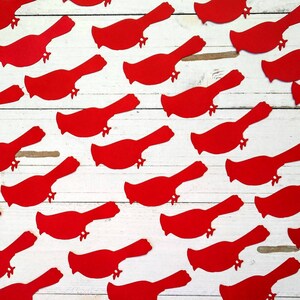 May include: A white wooden surface with red paper cutouts of cardinal birds scattered across it.