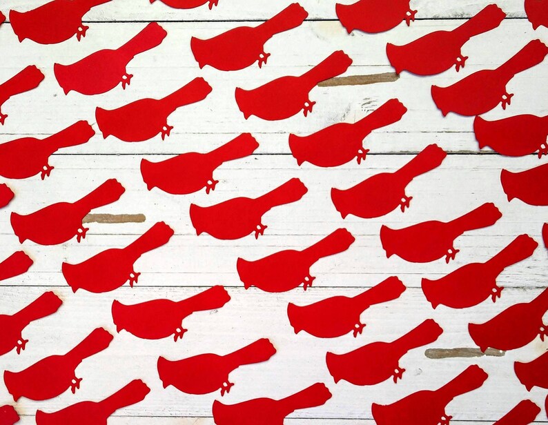 May include: A white wooden surface with red paper cutouts of cardinal birds scattered across it.
