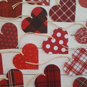 May include: A garland of red and white paper hearts with different patterns, including plaid, polka dots, and paisley. The hearts are strung together with twine.