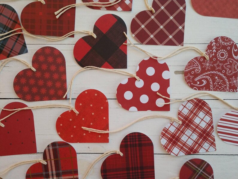 May include: A garland of red and white paper hearts with different patterns, including plaid, polka dots, and paisley. The hearts are strung together with twine.