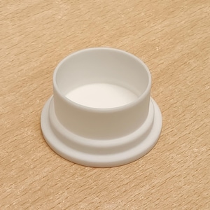 May include: A white plastic end cap featuring a cylindrical top section and a wider, circular base with a stepped design. The component has a smooth, matte finish and a hollow interior, designed to fit over or into a circular opening or tube.