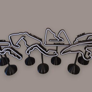 May include: A collection of six black and white 3D printed Formula 1 race track sculptures, each mounted on a circular base. The tracks feature the names Monza, Silverstone, Bahrain, and Miami clearly labelled on the black structural frames.