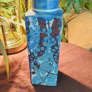 May include: A rectangular ceramic vase with a blue and brown floral pattern. The vase has a square base and a slightly narrower neck with a blue rim. The design features a repeating pattern of blue flowers and brown accents.