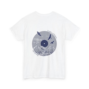 May include: A white ceramic mug with a black handle and the text "But First, Coffee" in a bold, black font. The mug is set against a blurred background, suggesting a cozy setting.