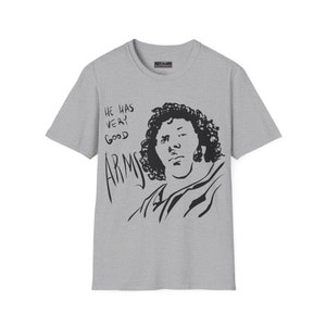 May include: A heather gray t-shirt featuring a black line drawing of a person with curly hair. The text "HE HAS VERY GOOD ARMS" is written in black above the drawing. The shirt has a crew neck and short sleeves.