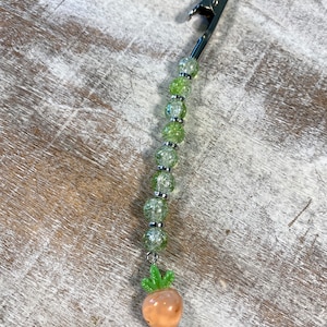 May include: A silver clip with a green and clear beaded chain and a peach-colored carrot charm.