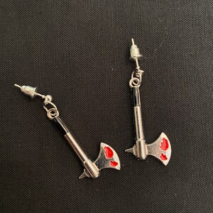 May include: A pair of silver axe earrings with red accents. The earrings are on a black background.