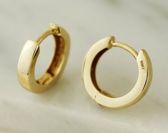 May include: A pair of gold-colored hoop earrings. The earrings are a simple, classic design with a smooth, polished finish. The text "Serena Sparkles" is in the upper center of the image. The earrings are marked "10KT".