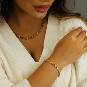 May include: A woman wearing a white sweater with a gold chain necklace and a gold rope chain bracelet. The bracelet is on her left wrist. The text "Serena Sparkles" is visible in the bottom right corner of the image.