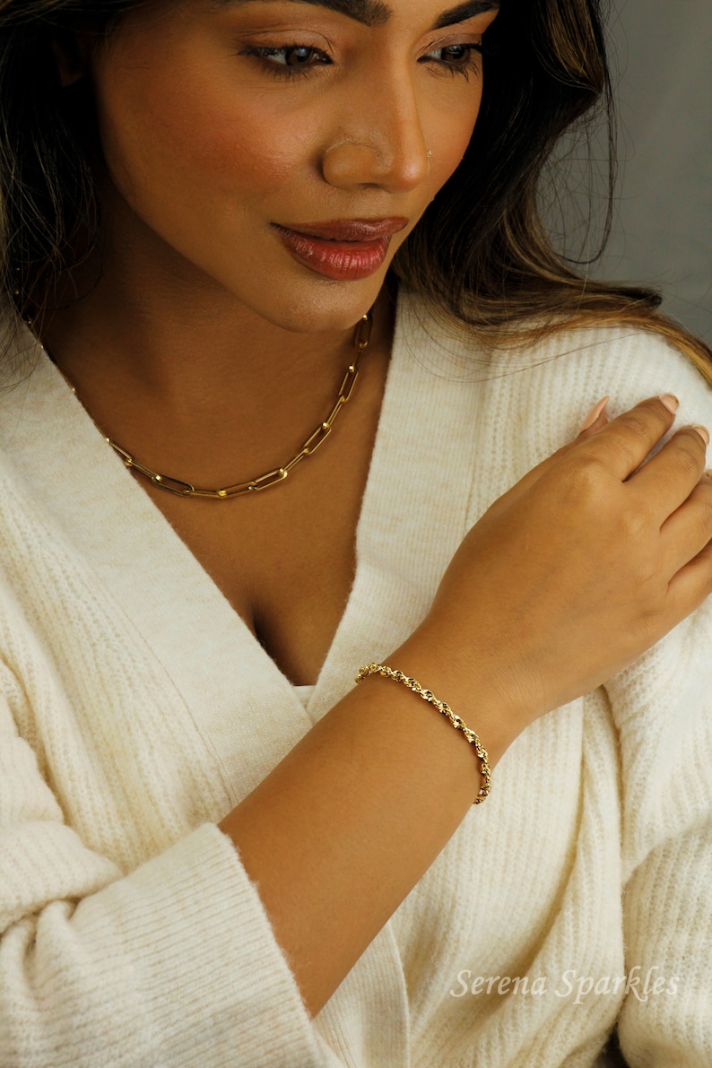 May include: A woman wearing a white sweater with a gold chain necklace and a gold rope chain bracelet. The bracelet is on her left wrist. The text "Serena Sparkles" is visible in the bottom right corner of the image.