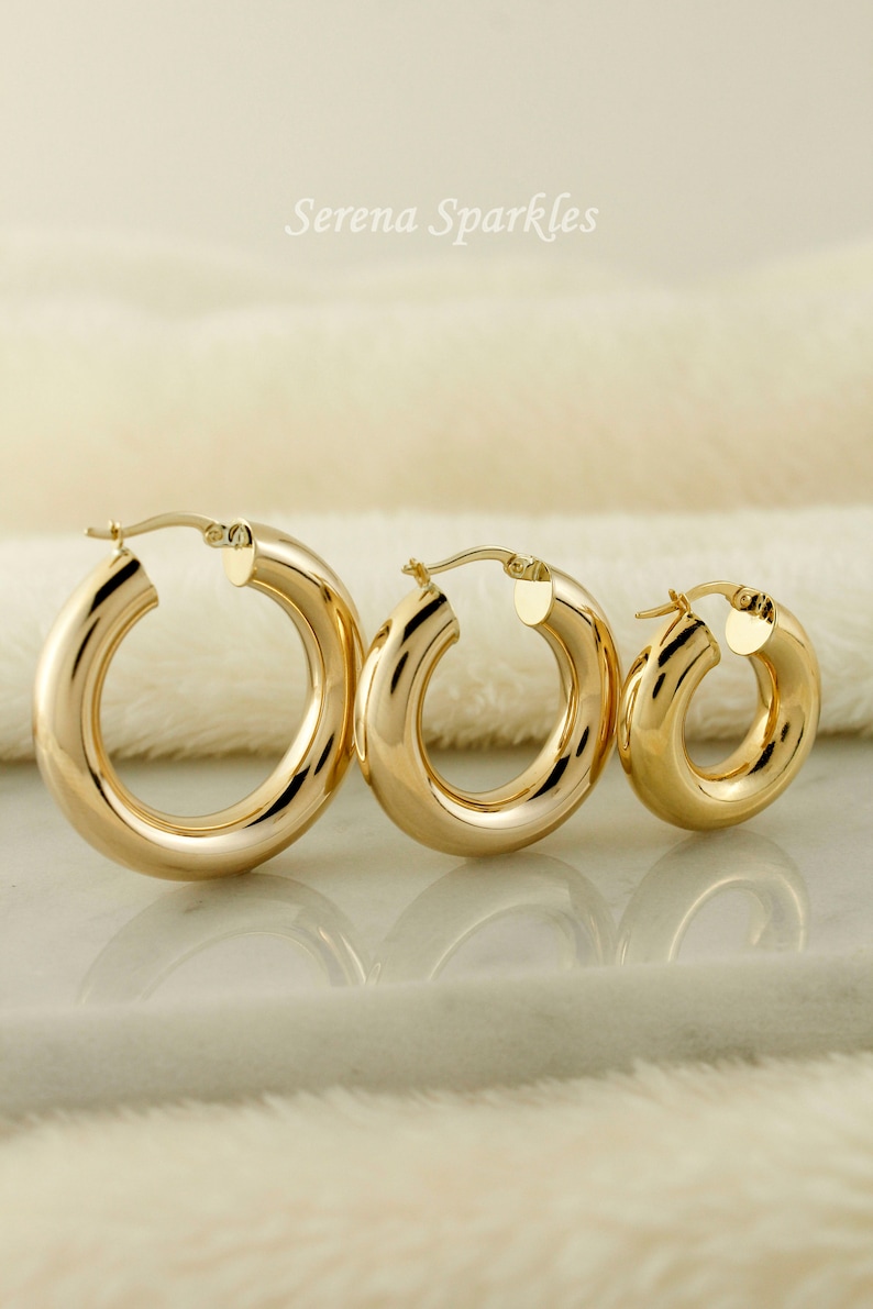 May include: Three gold hoop earrings of different sizes. The largest hoop is on the left, the medium hoop is in the middle, and the smallest hoop is on the right.