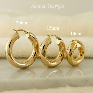 May include: Three gold hoop earrings of different sizes, 20mm, 15mm, and 10mm, on a white fuzzy surface.