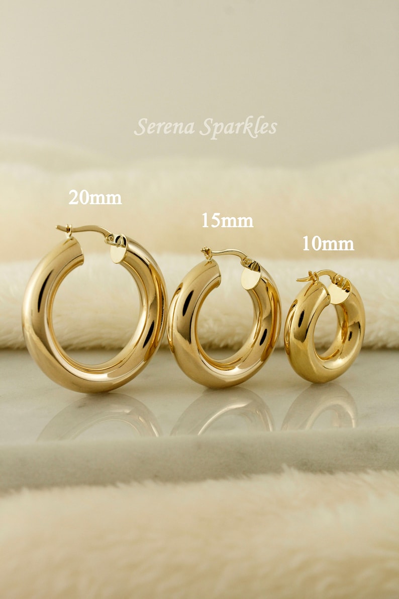 May include: Three gold hoop earrings of different sizes, 20mm, 15mm, and 10mm, on a white fuzzy surface.