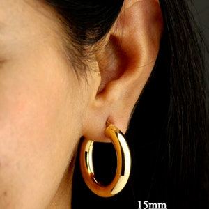 May include: Gold hoop earrings with a 1.5 inch diameter. The earrings are shown on a person's ear.