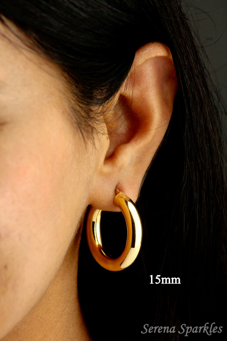 May include: Gold hoop earrings with a 1.5 inch diameter. The earrings are shown on a person's ear.