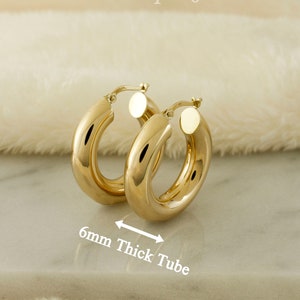 May include: Gold hoop earrings with a thick tube design. The earrings are 6mm thick.