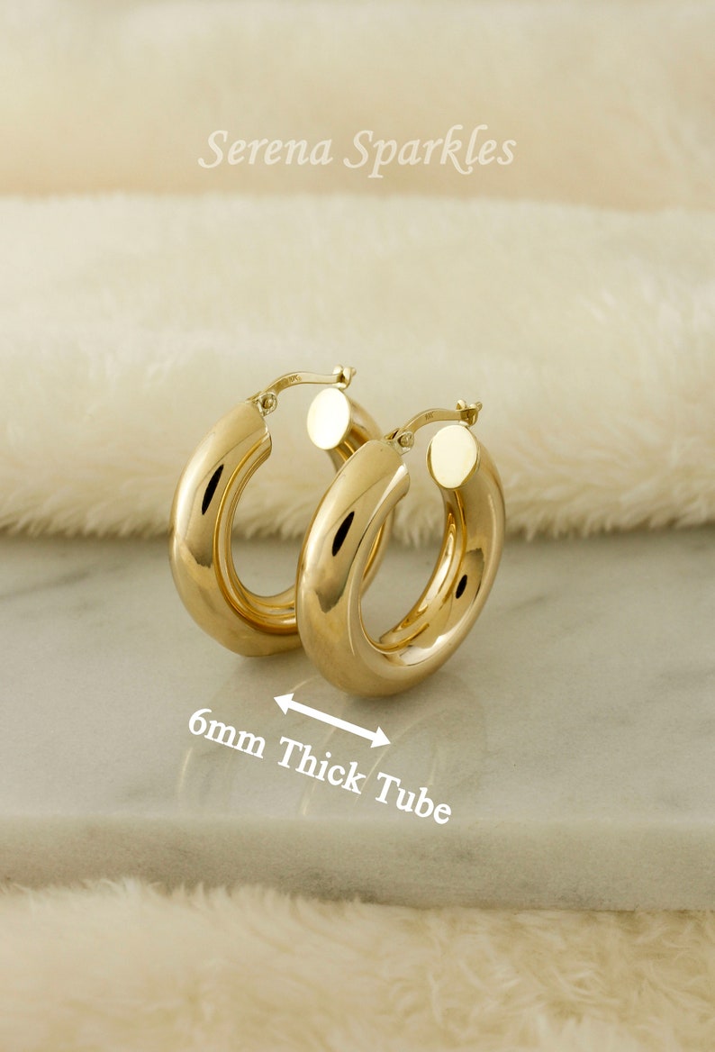 May include: Gold hoop earrings with a thick tube design. The earrings are 6mm thick.