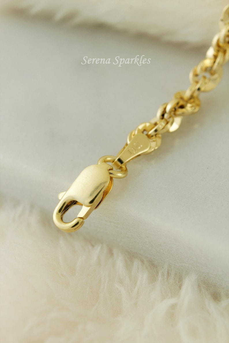 May include: Close-up of a gold chain necklace with a lobster clasp. The chain is made of small, round links.