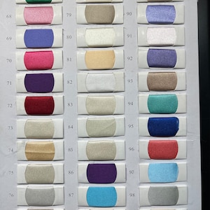 K&ouml;nnte beinhalten: Eine Stofffarbkarte mit dreiunddrei&szlig;ig rechteckigen Mustern, die in drei vertikalen Spalten angeordnet sind. Jedes Muster ist von 67 bis 99 nummeriert und zeigt eine eigene Farbe mit Satin-Finish, darunter Gr&uuml;n-, Rosa-, Blau-, Lila-, Rot-, Gold-, Silber- und Beiget&ouml;ne.