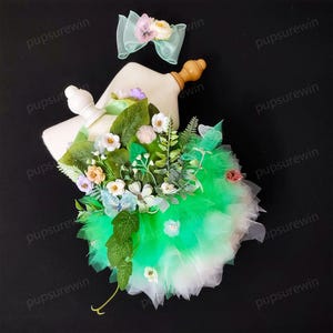 May include: A green and white tulle tutu with a floral embellishment. The flowers are made of fabric and include butterflies, leaves, and small white flowers. The tutu is on a white mannequin.