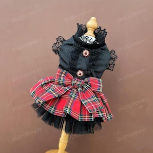 May include: A black and red plaid dog dress with a black lace collar and a black bow. The dress has a tulle skirt and is decorated with rhinestones.