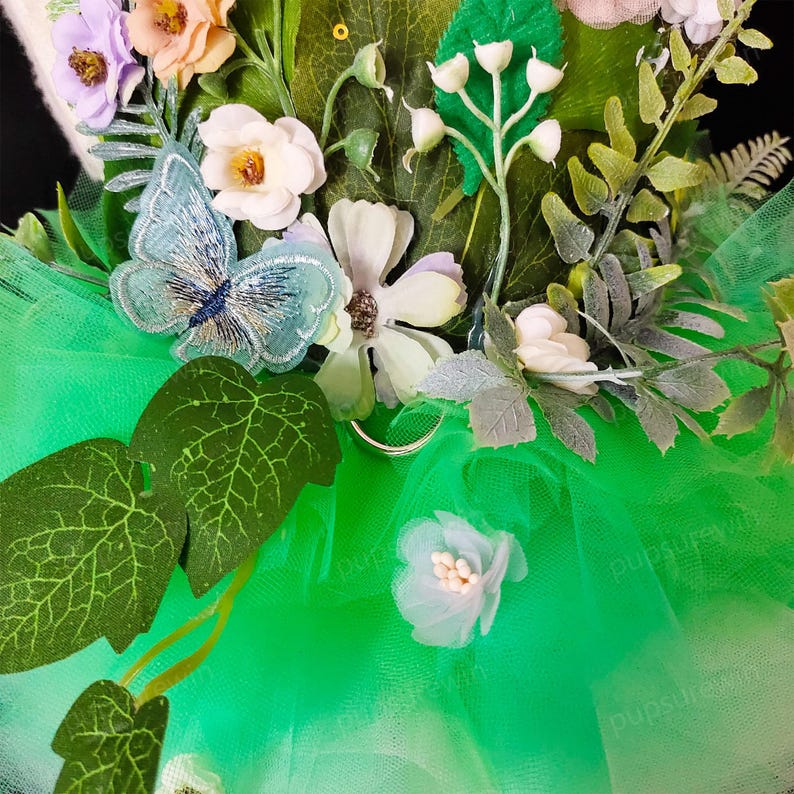 May include: A green tulle tutu with a floral embellishment featuring a blue butterfly, white flowers, and green leaves.