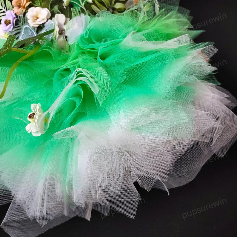 May include: A green and white tulle fabric with a gradient effect. The fabric is ruffled and layered, creating a soft and delicate look.