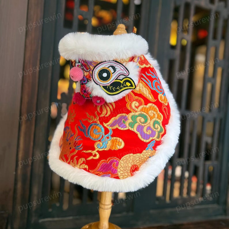 May include: Red and gold Chinese lion dance costume for a pet, with white fur trim and a pink nose.