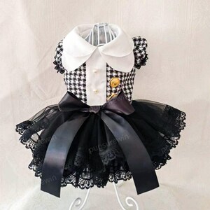 K&ouml;nnte beinhalten: Ein schwarz-wei&szlig; kariertes Kleid mit wei&szlig;em Kragen und schwarzer Schleife. Das Kleid hat einen schwarzen T&uuml;llrock mit Spitzenbesatz.