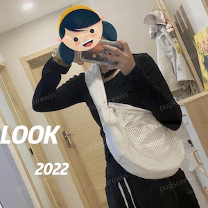 May include: A white mesh bag with a heart-shaped opening. The bag is worn as a crossbody bag and has a zipper closure. The bag is made of a soft, textured fabric.