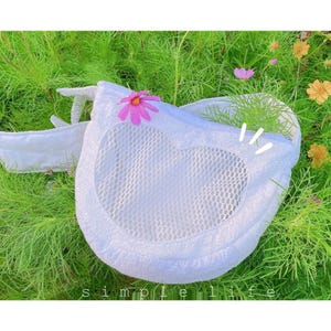 May include: White mesh bag with a heart-shaped opening and a pink flower design. The bag is lying on a bed of green grass.