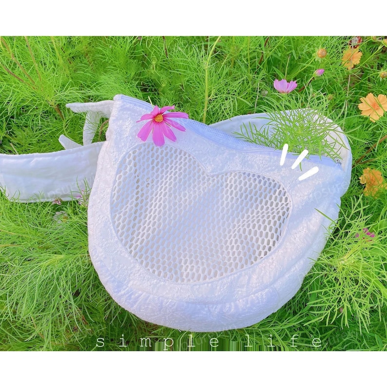 May include: White mesh bag with a heart-shaped opening and a pink flower design. The bag is lying on a bed of green grass.