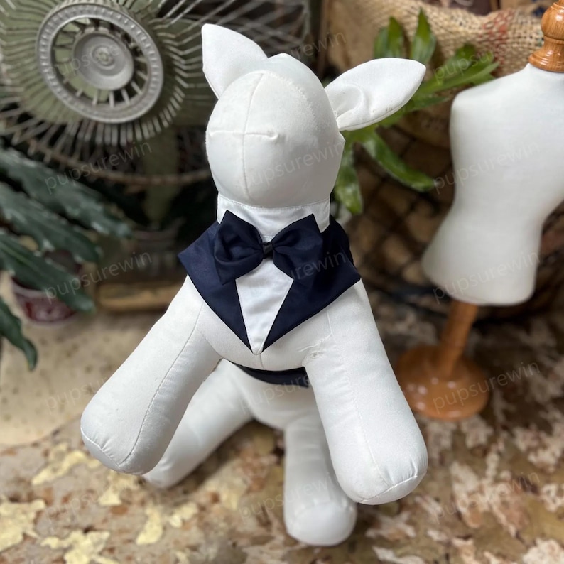 K&ouml;nnte beinhalten: Eine wei&szlig;e Stoff-Tierpuppe in Hundeform, ausgestattet mit einem dunkelblauen Smoking-Kragen und einer passenden Fliege. Die Puppe hat aufrecht stehende Ohren und eine glatte, gepolsterte Oberfl&auml;che, die zur Pr&auml;sentation von Tierzubeh&ouml;r dient.