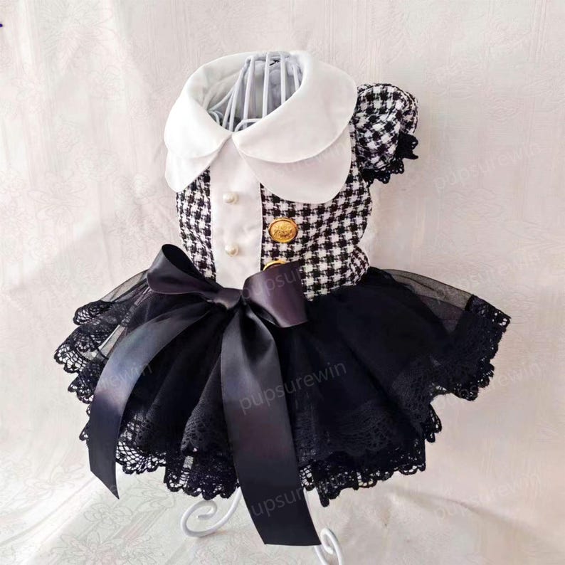 K&ouml;nnte beinhalten: Ein schwarz-wei&szlig; kariertes Kleid mit wei&szlig;em Kragen und einer schwarzen Schleife. Das Kleid hat einen schwarzen T&uuml;llrock mit Spitzenbesatz.
