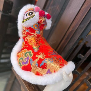 May include: Red and gold Chinese dragon costume for a pet. The costume has a white fur trim and a lion head with a white fur mane.