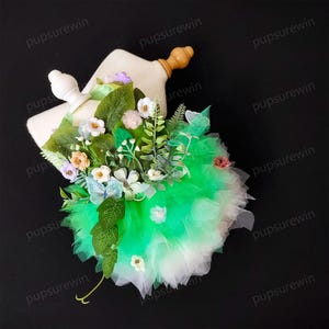 May include: A green and white tulle tutu with a floral embellishment. The embellishment features a variety of flowers, leaves, and butterflies.