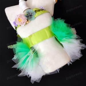 May include: A green and white tulle dog tutu with a lime green satin ribbon and floral embellishments. The tutu is on a white mannequin.