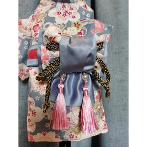 Pu&ograve; includere: Un kimono per cani blu e bianco a fiori con una cintura in raso blu e nappe rosa. La cintura &egrave; legata con un fiocco con un cordoncino intrecciato dorato.