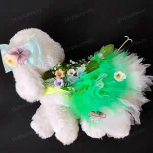 May include: A white plush dog wearing a green tulle dress with floral and butterfly embellishments.