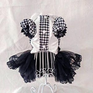 K&ouml;nnte beinhalten: Ein schwarz-wei&szlig; kariertes Kleid mit einem wei&szlig;en Satin-Oberteil und einem schwarzen T&uuml;llrock mit Spitzenbesatz. Das Kleid steht auf einem wei&szlig;en St&auml;nder.