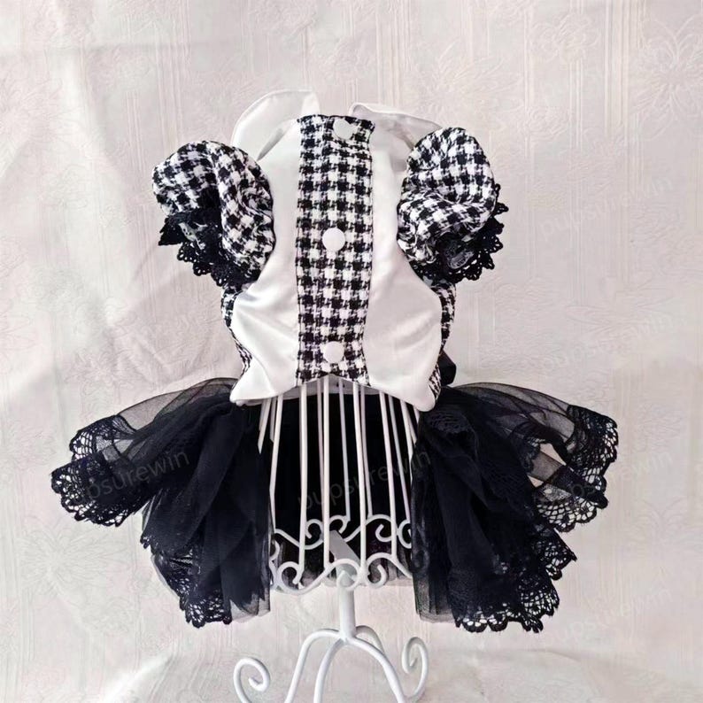K&ouml;nnte beinhalten: Ein schwarz-wei&szlig; kariertes Kleid mit einem wei&szlig;en Satin-Oberteil und einem schwarzen T&uuml;llrock mit Spitzenbesatz. Das Kleid steht auf einem wei&szlig;en St&auml;nder.