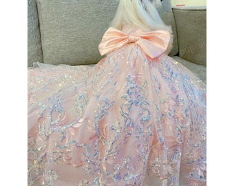 May include: A small white dog wearing a pink tulle dress with a large pink bow and iridescent sequins. The dress has a floral pattern and is perfect for a special occasion.