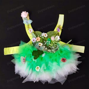 May include: A green and white tulle tutu with a yellow bodice. The bodice is decorated with a floral arrangement of green leaves, pink, white, and purple flowers, and butterflies.