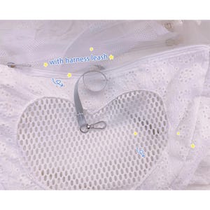 May include: White mesh pet carrier with a heart-shaped opening and a zipper closure. The carrier has a white lace trim and a gray leash with a clip attached. The text "with harness leash" is written on the carrier.