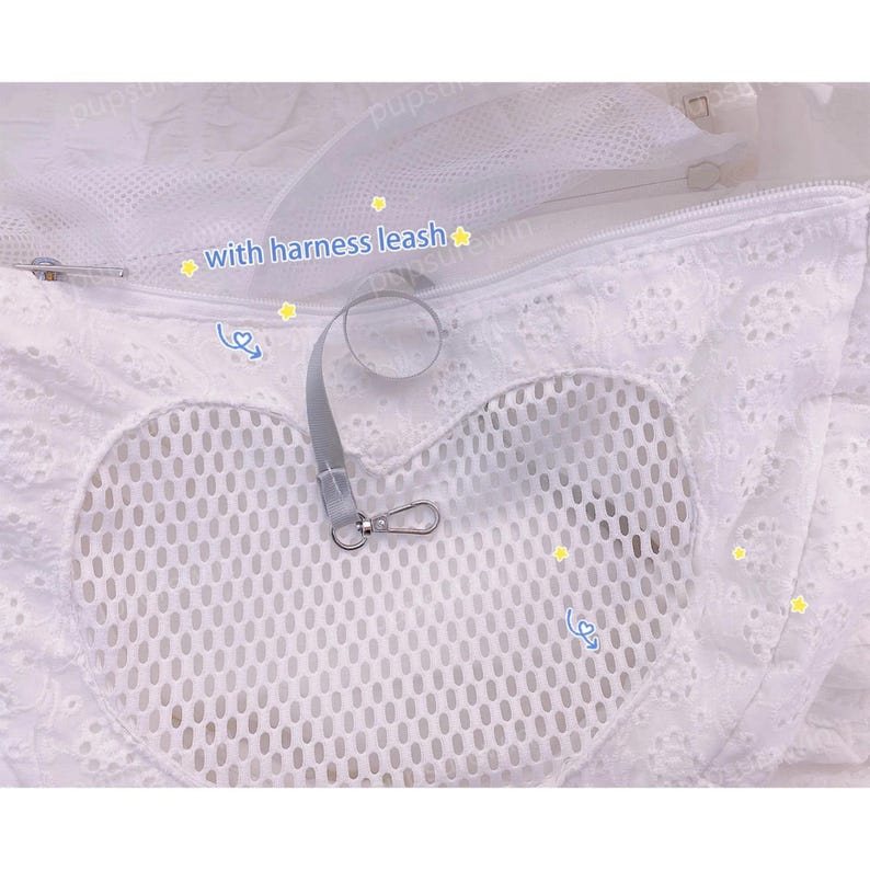 May include: White mesh pet carrier with a heart-shaped opening and a zipper closure. The carrier has a white lace trim and a gray leash with a clip attached. The text "with harness leash" is written on the carrier.