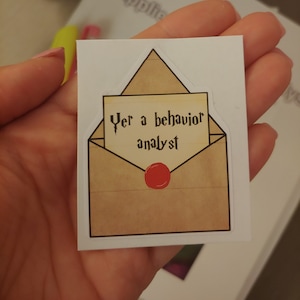 May include: A brown envelope with a red wax seal. The envelope has a white paper inside with the text "Yer a behavior analyst" written in black.