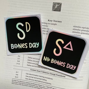May include: Two black square stickers with iridescent edges. One reads "SD BONES DAY" in white script, the other reads "SA NO BONES DAY". The stickers are on a textbook page with the title "Stimulus Control".