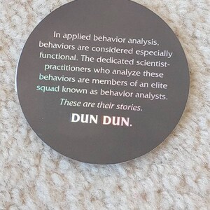 May include: A round sticker with a dark gray background and white text. The text reads: "In applied behavior analysis, behaviors are considered especially functional. The dedicated scientist-practitioners who analyze these behaviors are members of an elite squad known as behavior analysts. These are their stories. DUN DUN."
